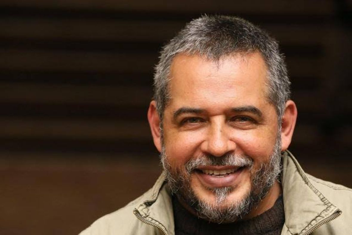 Homem de casaco bege sorrindo em retrato