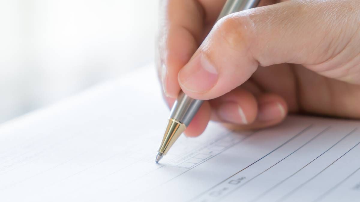 A hand filling in a paper questionnaire with a pen