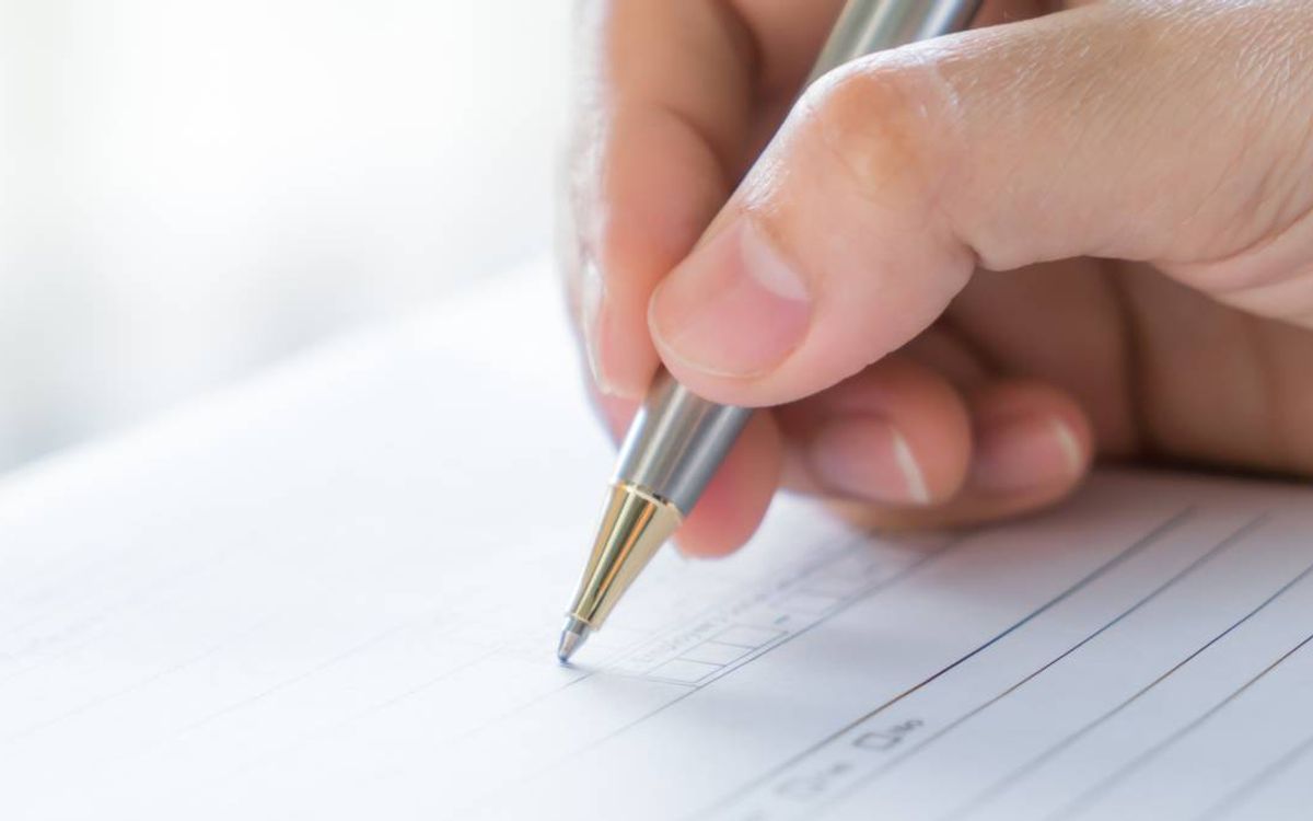 A hand filling in a paper questionnaire with a pen