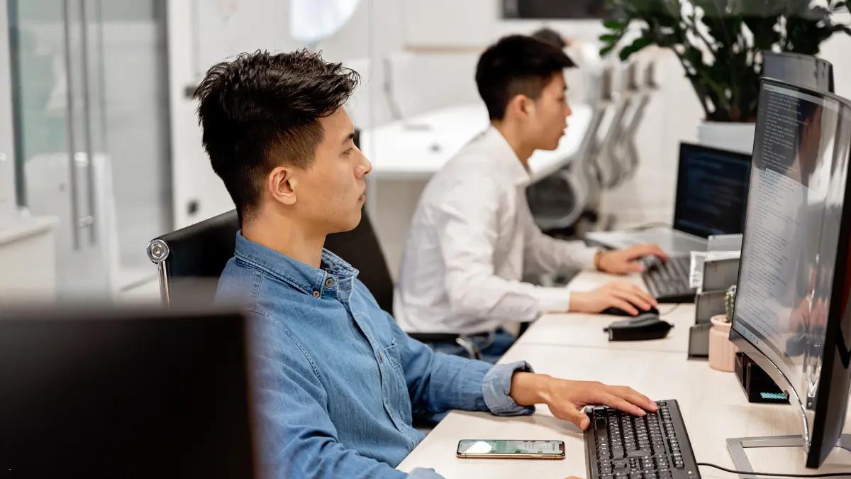 Two analysts working at desktop monitors in an open office
