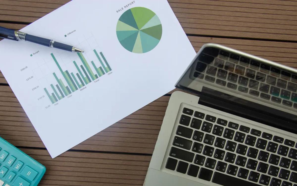 A printed report with bar and pie charts beside a laptop, a pen and a calculator