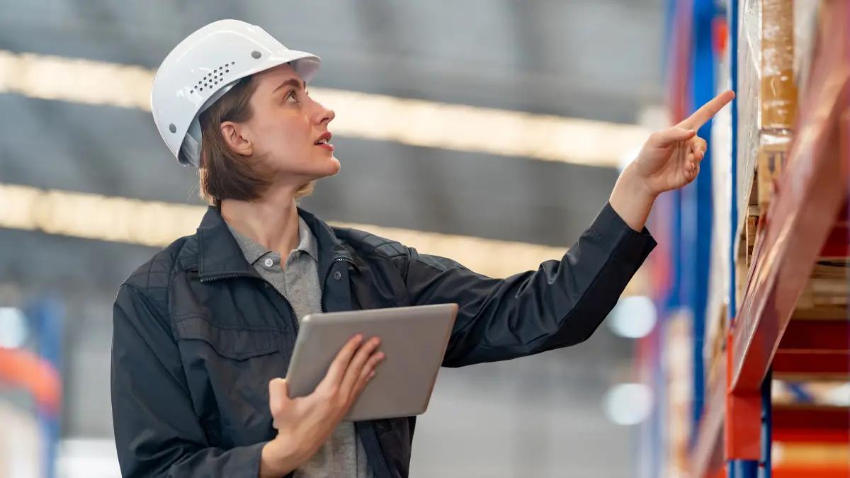 Warehouse worker in a hard hat holding a tablet and pointing at pallet racking
