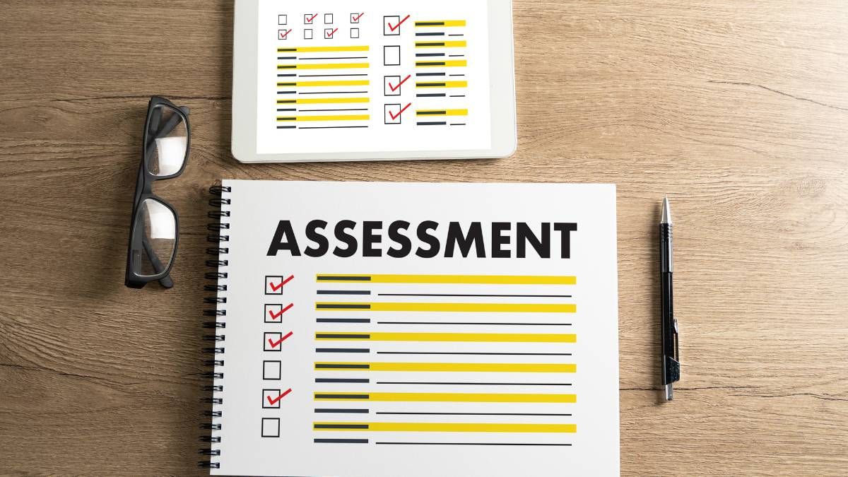 Printed assessment checklist with highlighted lines beside glasses, a pen and a tablet