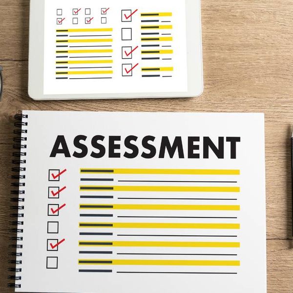 Printed assessment checklist with highlighted lines beside glasses, a pen and a tablet