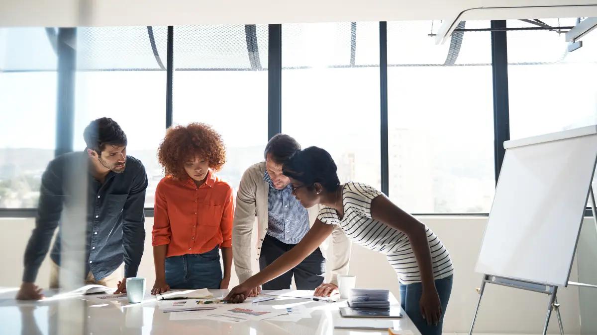 Four colleagues leaning over printed reports on a conference table