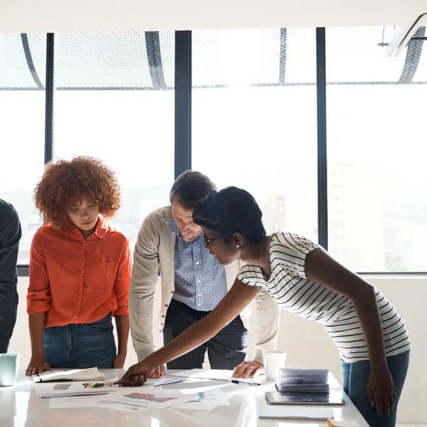 Four colleagues leaning over printed reports on a conference table
