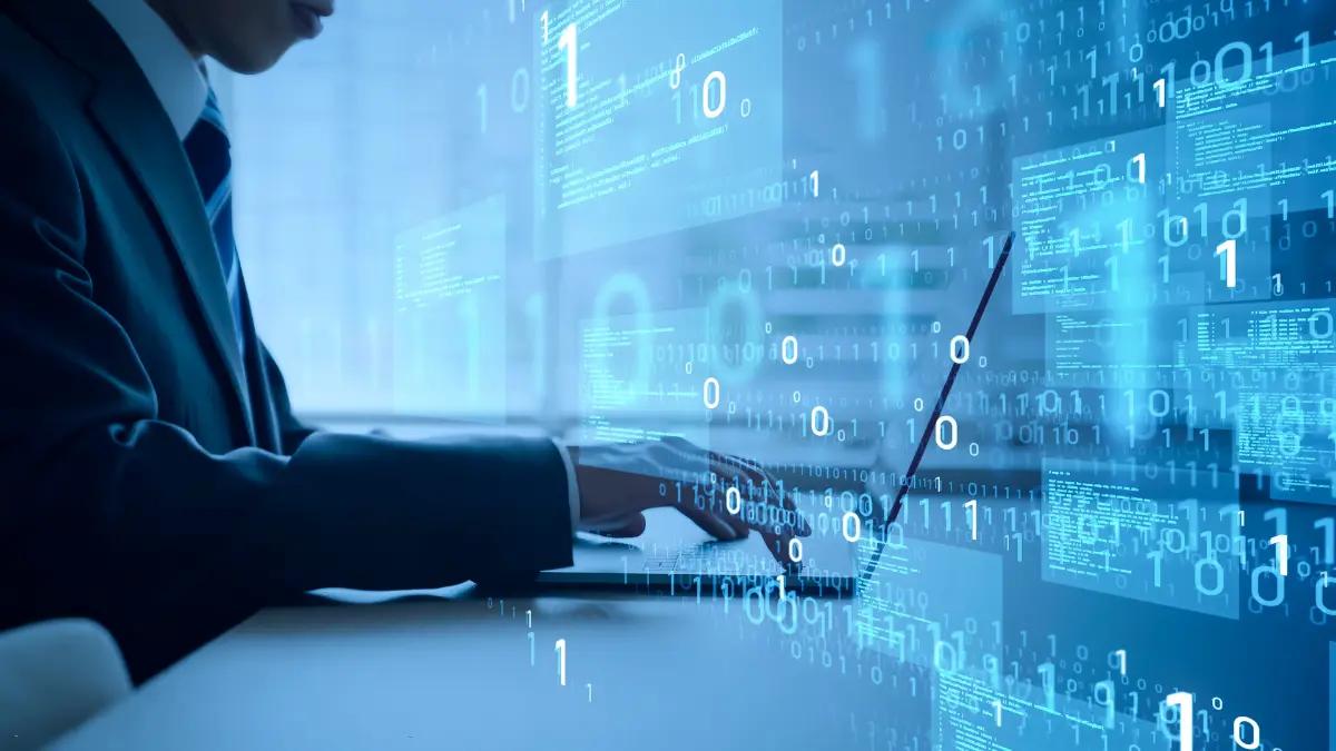 A person in a suit typing on a laptop with streams of binary data overlaid on the screen