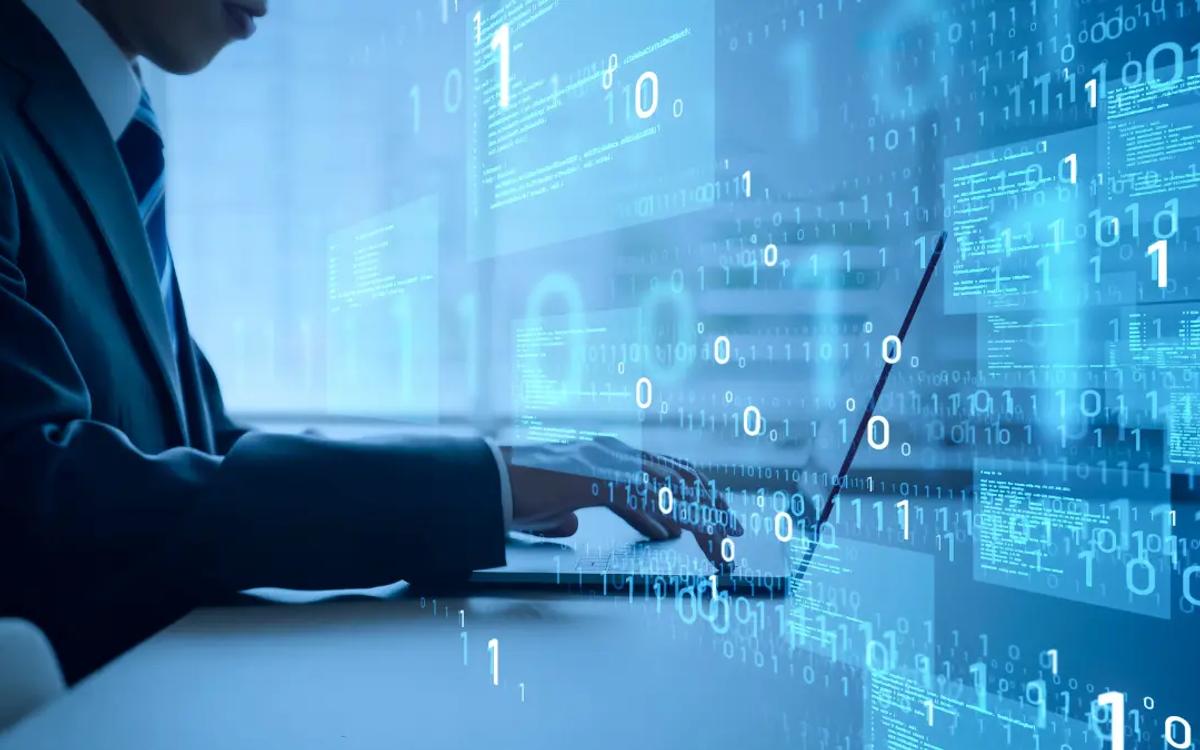 A person in a suit typing on a laptop with streams of binary data overlaid on the screen