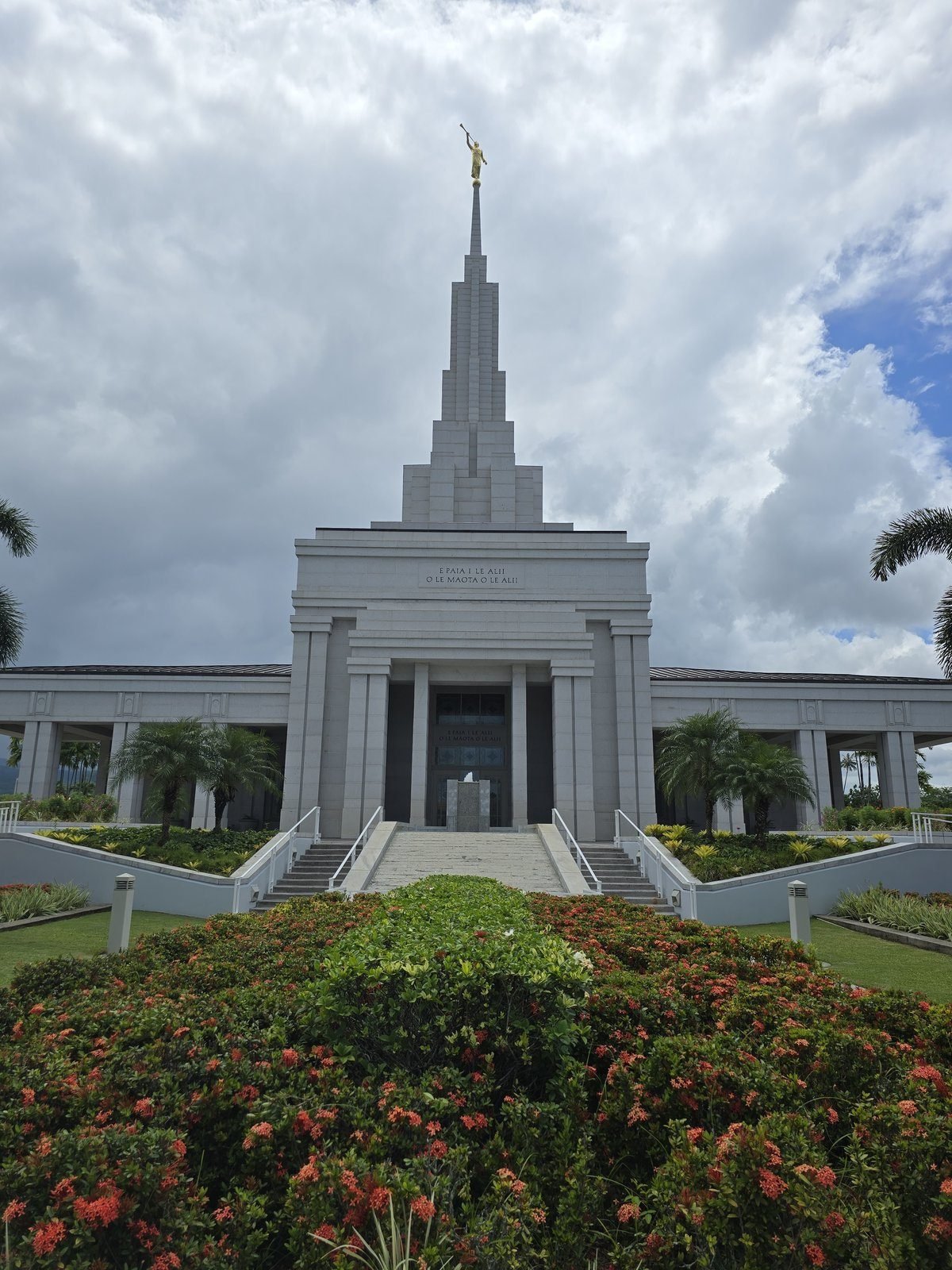 The white spire of the Apia Samoa Temple above red flower beds
