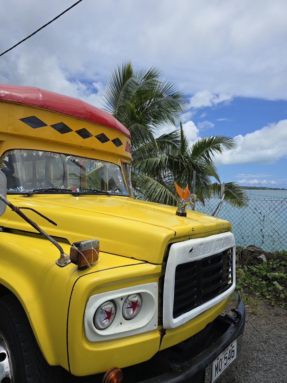 A yellow Samoan island bus parked under palms