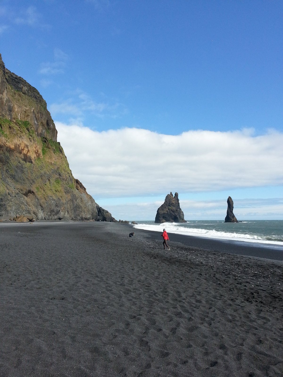 The black sand beach at Reynisfjara with the Reynisdrangar stacks and a lone figure in red