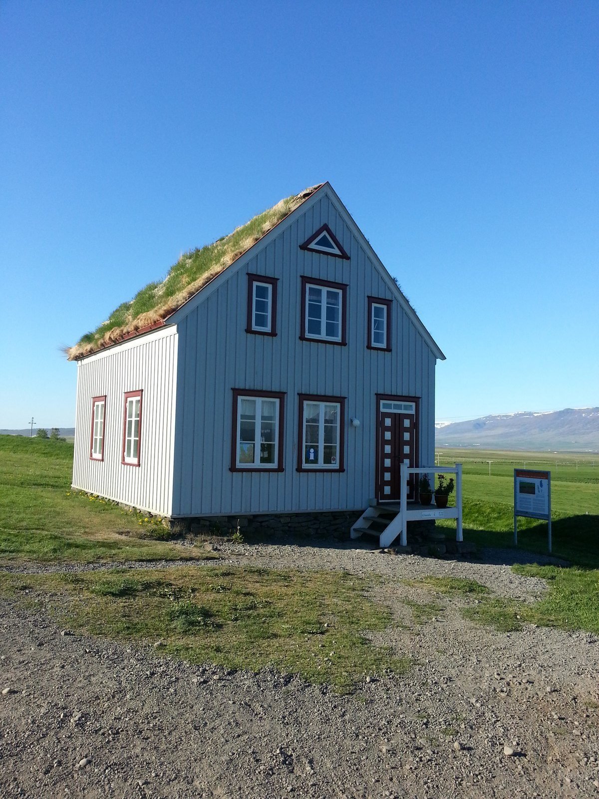 A blue-and-white Icelandic house with a turf roof under an open sky