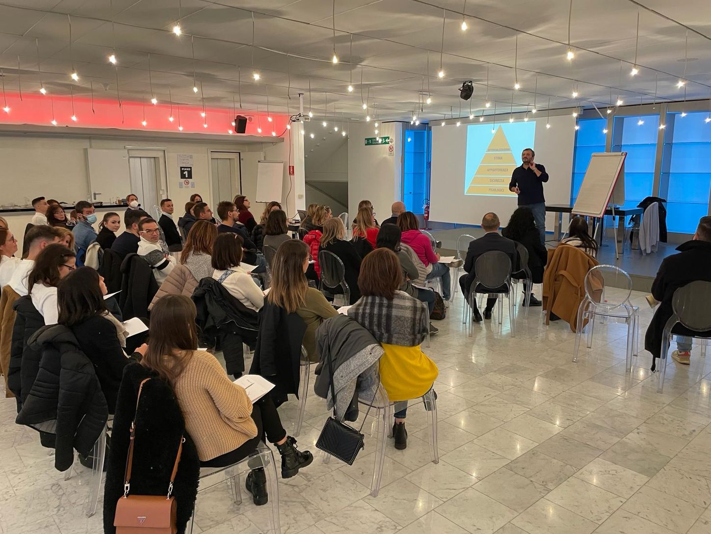 Uomo su un palco che parla di fronte ad un pubblico di persone sedute