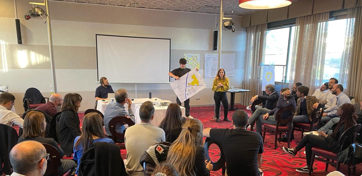 Due persone che presentano un progetto davanti ad un pubblico seduto