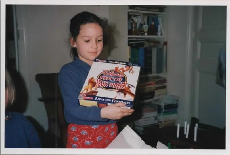 Élise enfant, découvrant un CD-ROM de jeux vidéo Disney avec émerveillement