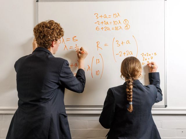 School Children in Uniform solving maths problem on a white board