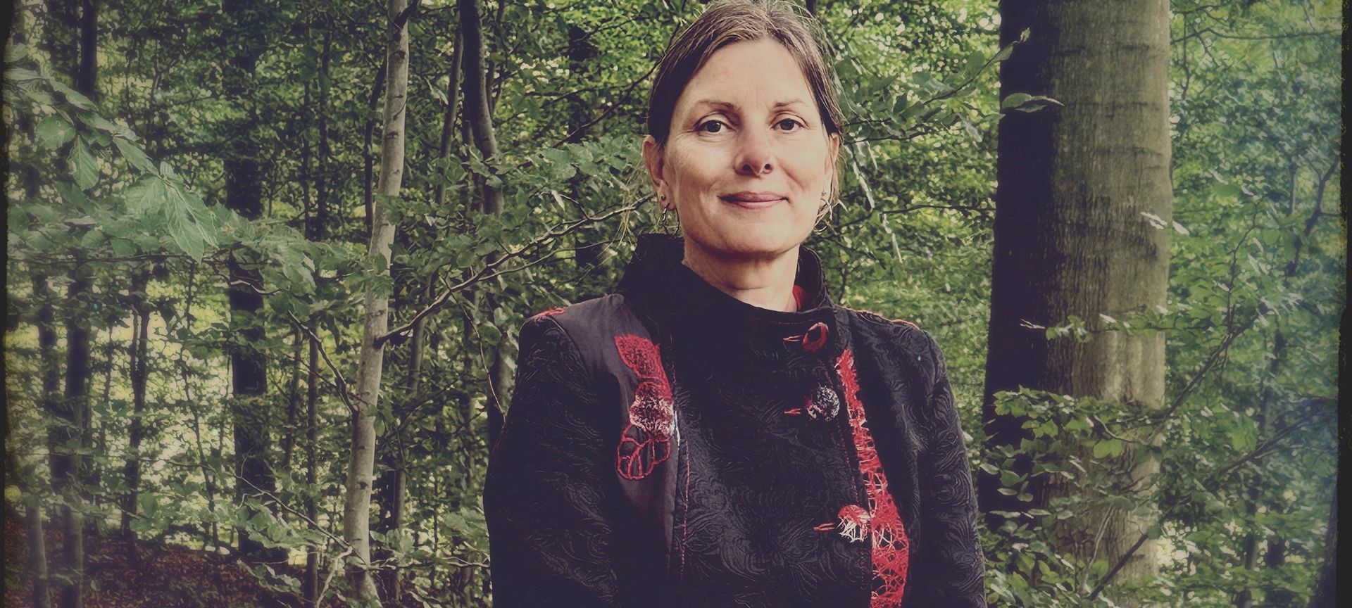 Zita Fejerskov Andersen står i et skovbryn i en mørk jakke med rødt broderi