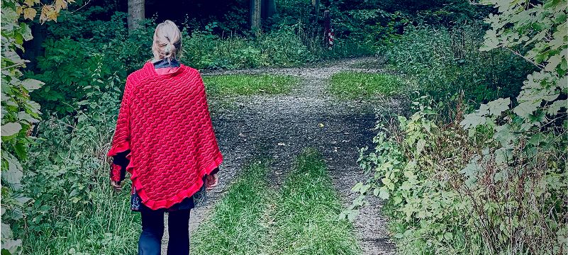 Kvinde i rød poncho går ad en grusti gennem skoven