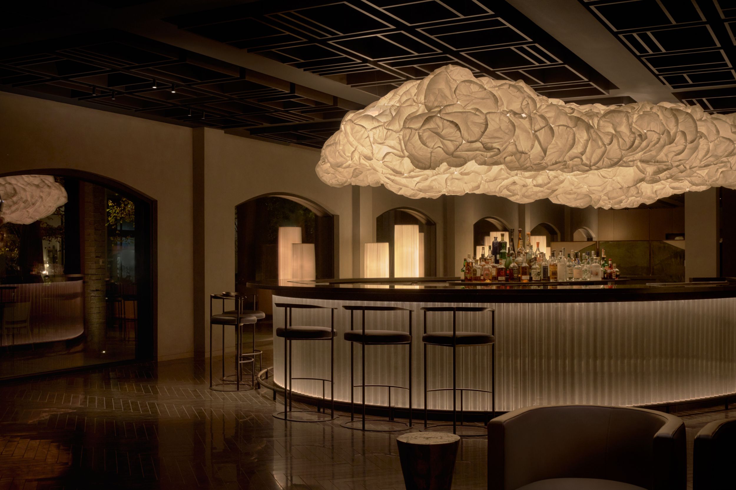 The close up of the curved area of the bar with Frank Gehry's MammaCloud light suspended above. The guest room inside AKA Alexandria. The seating area alongside the glass wall of the restaurant of AKA Alexandria.  | AKA Hotel Alexandria | Alexandria, Virginia, USA | Architecture and Interiors by Lissoni Partners | Photography by Veeral Patel
