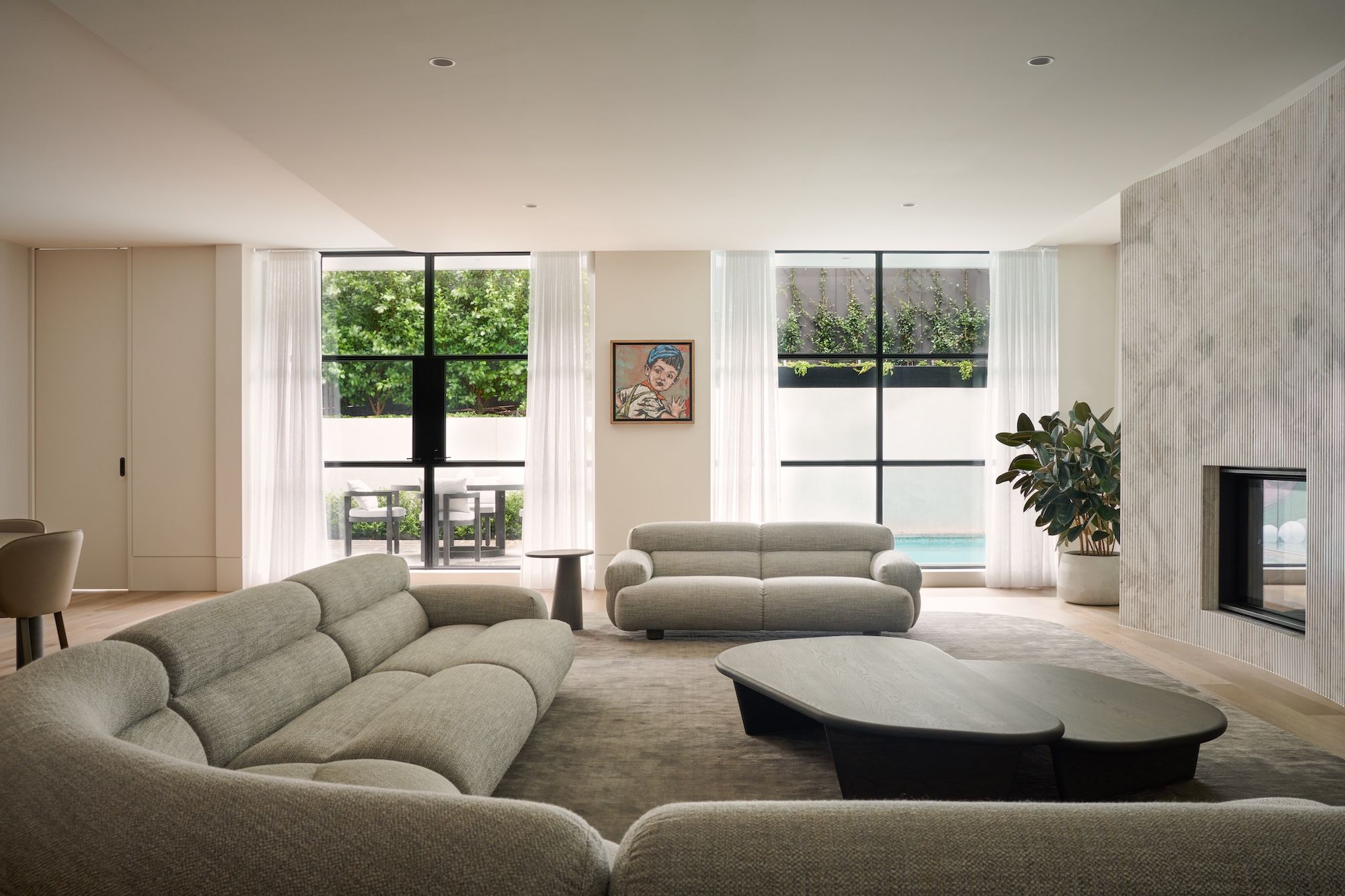 An elevation view of the living room with Valley sofas designed by Jardan and, showing the rear courtyard with a small swimming pool.  | Straun Residences interior architecture by Mim Design and built by Virgon Constructions | Mim Design | Toorak, Victoria | Architectural Photography Veeral Patel