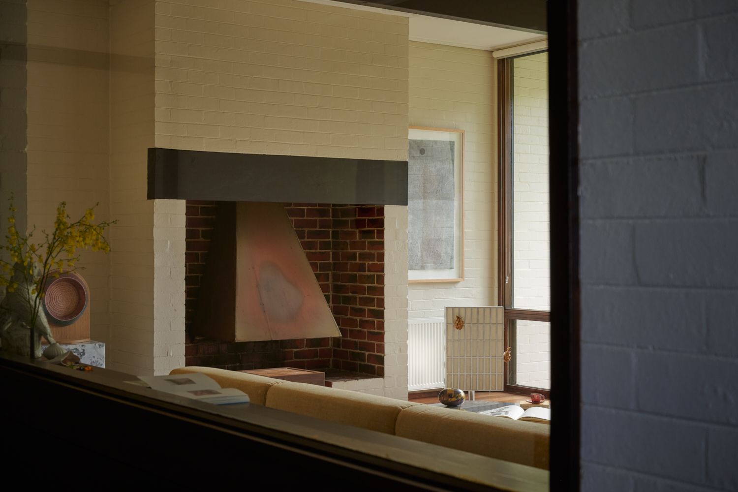 A glimpse into the living through the glass in the hallway, showing the copper shroud of the fireplace. A garden view of Wildwood showing the depth of the colonnades. | Wildwood design by Robin Boyd | Vermont, Victoria | Midcentury Architecture | Architectural Photography by Veeral Patel 