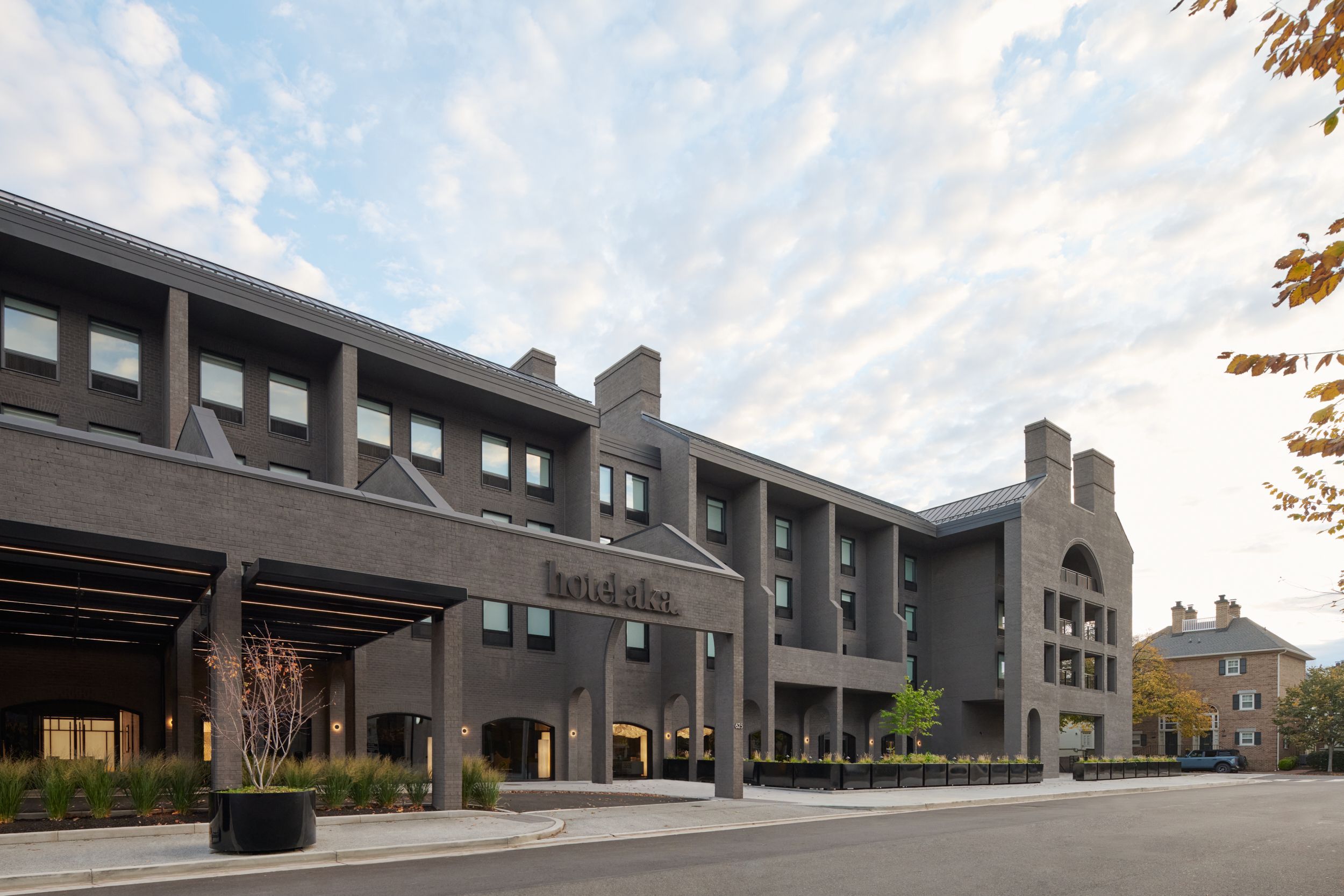 The external architectural view of AKA Alexandria. The former red bricks painted grey. The guest room inside AKA Alexandria. The seating area alongside the glass wall of the restaurant of AKA Alexandria.  | AKA Hotel Alexandria | Alexandria, Virginia, USA | Architecture and Interiors by Lissoni Partners | Photography by Veeral Patel