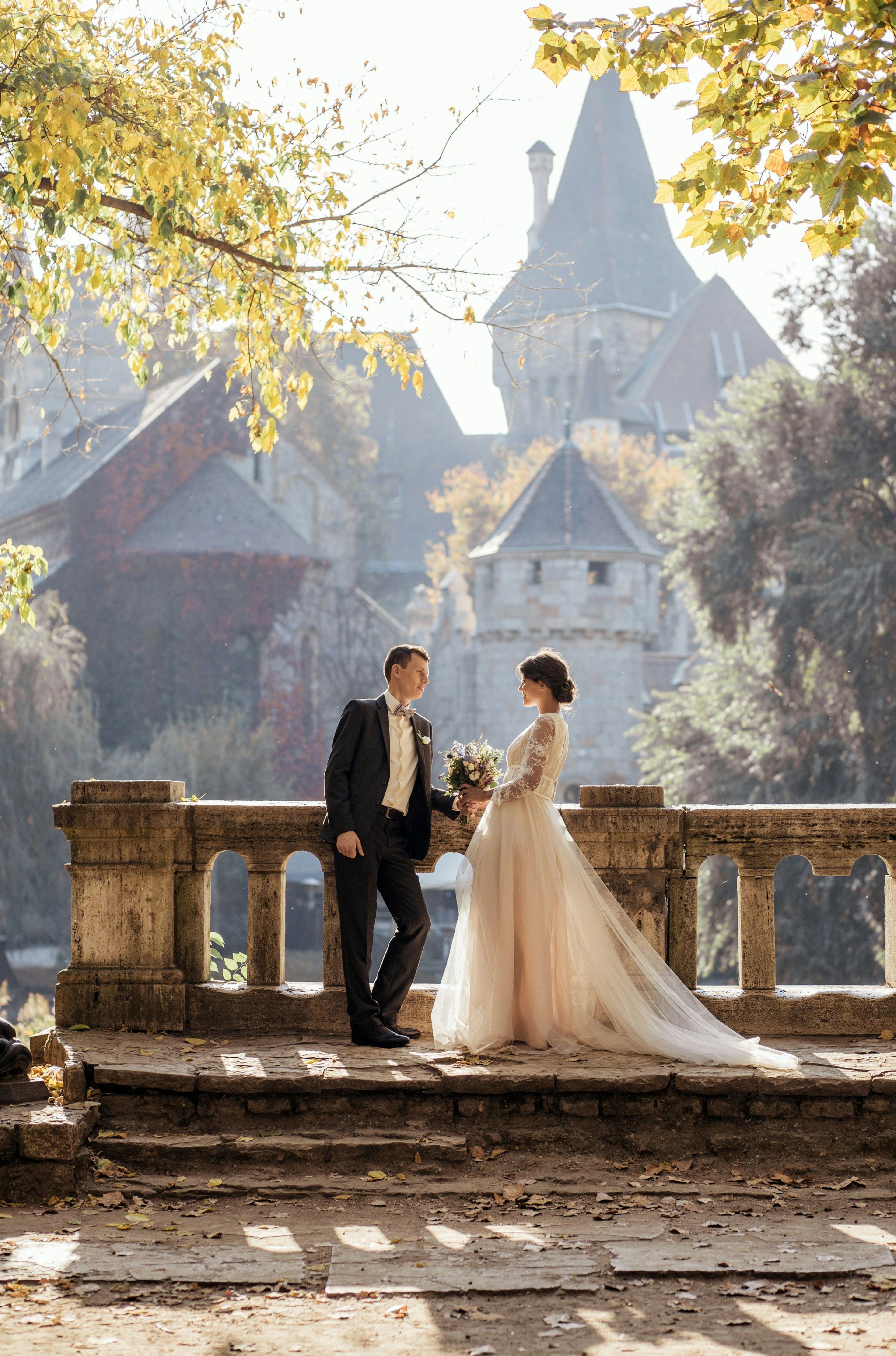 Couple in wedding attire on a stone bridge among autumn trees