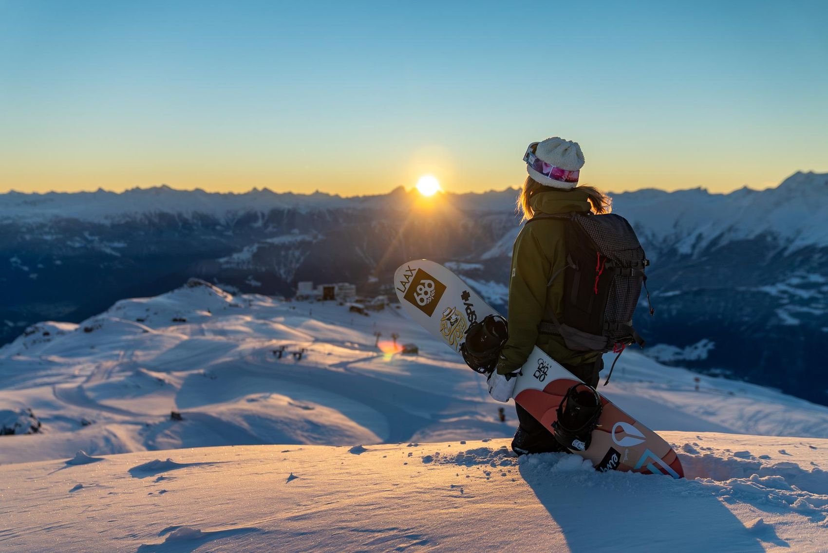 Snowboarderin steht im Tiefschnee und blickt in den Sonnenuntergang