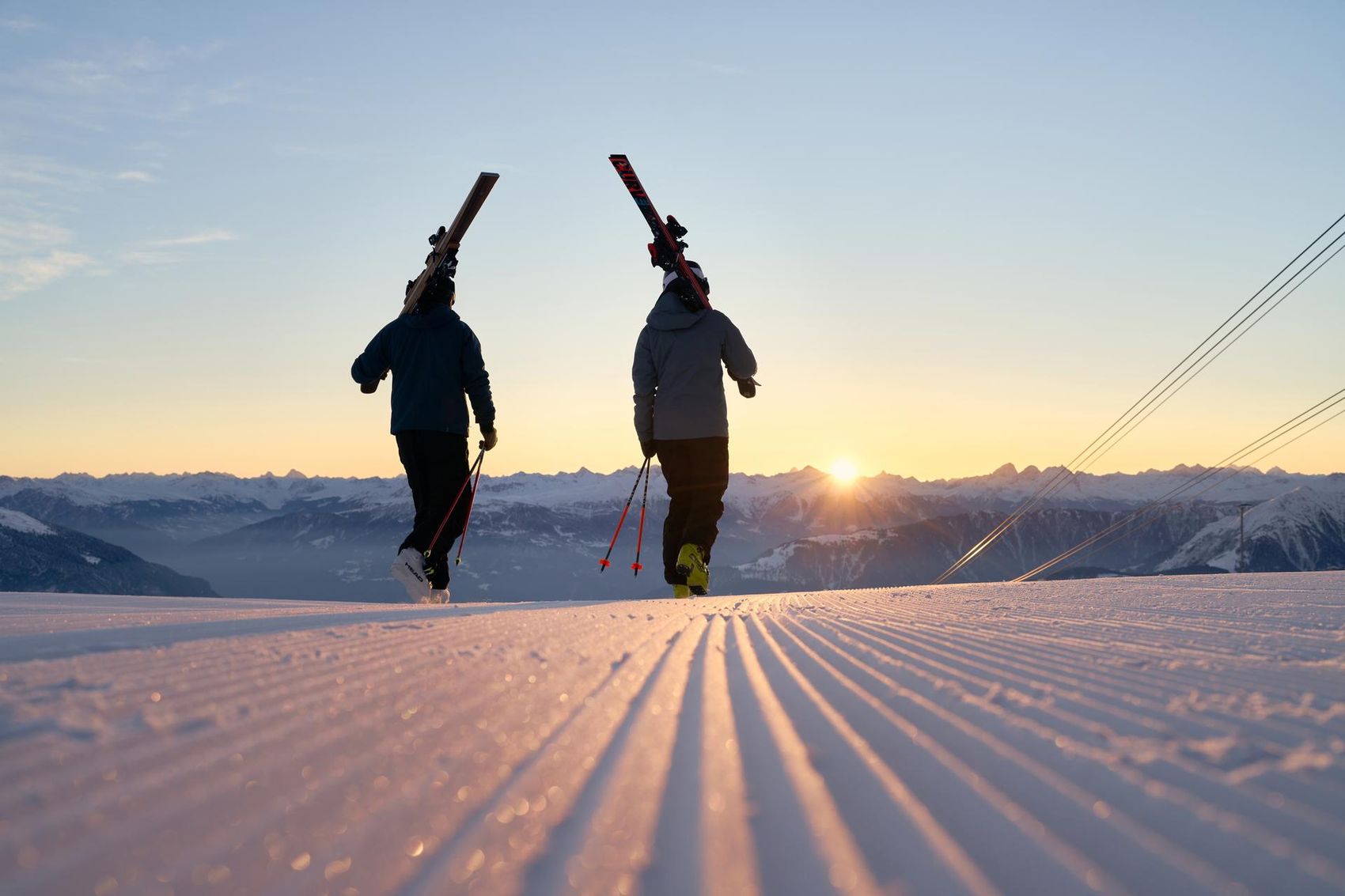 Skiers walk with their skis into the sunrise