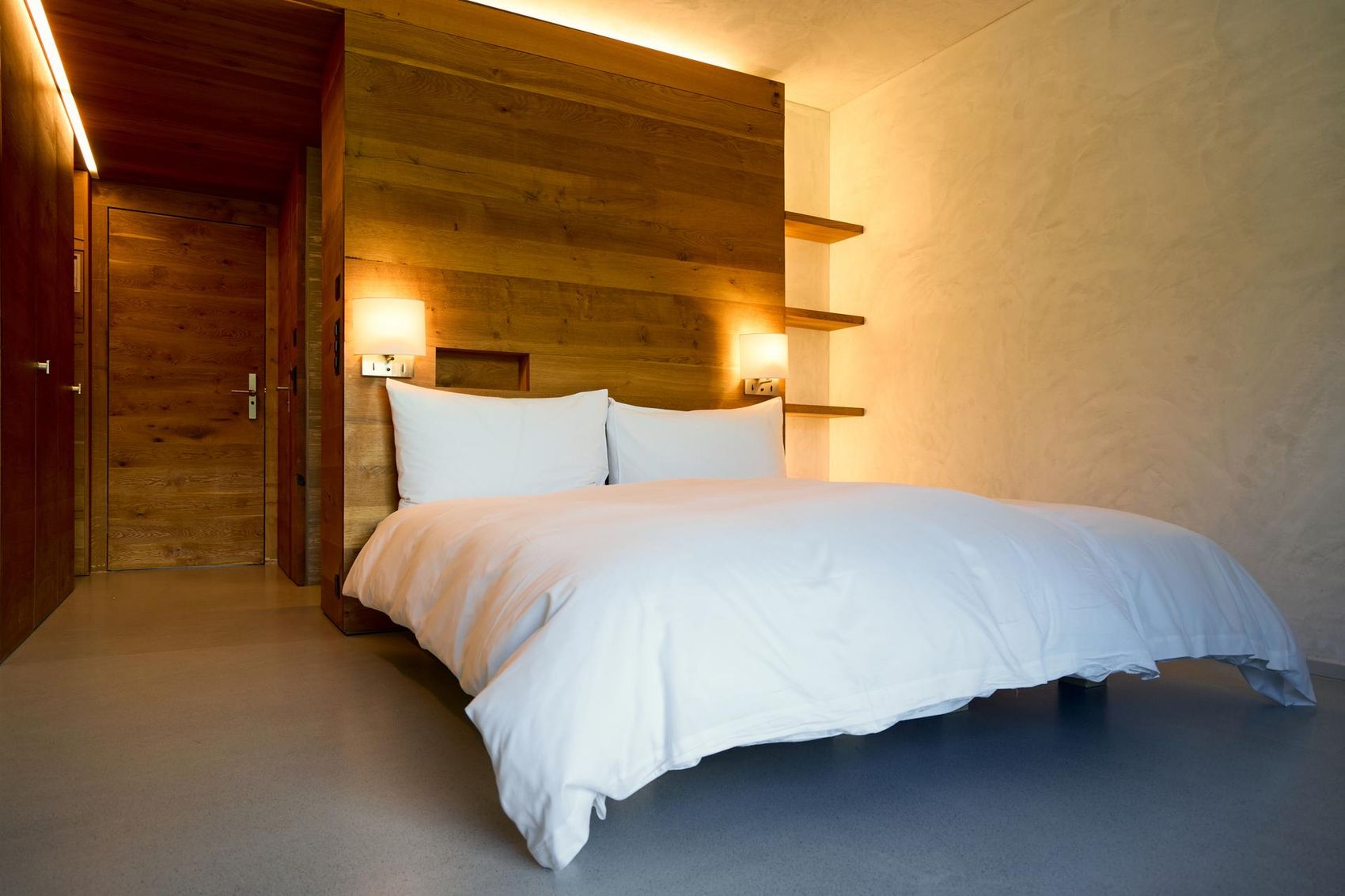 Weiss bezogenes Hotelbett mit Holzwand im Hintergrund