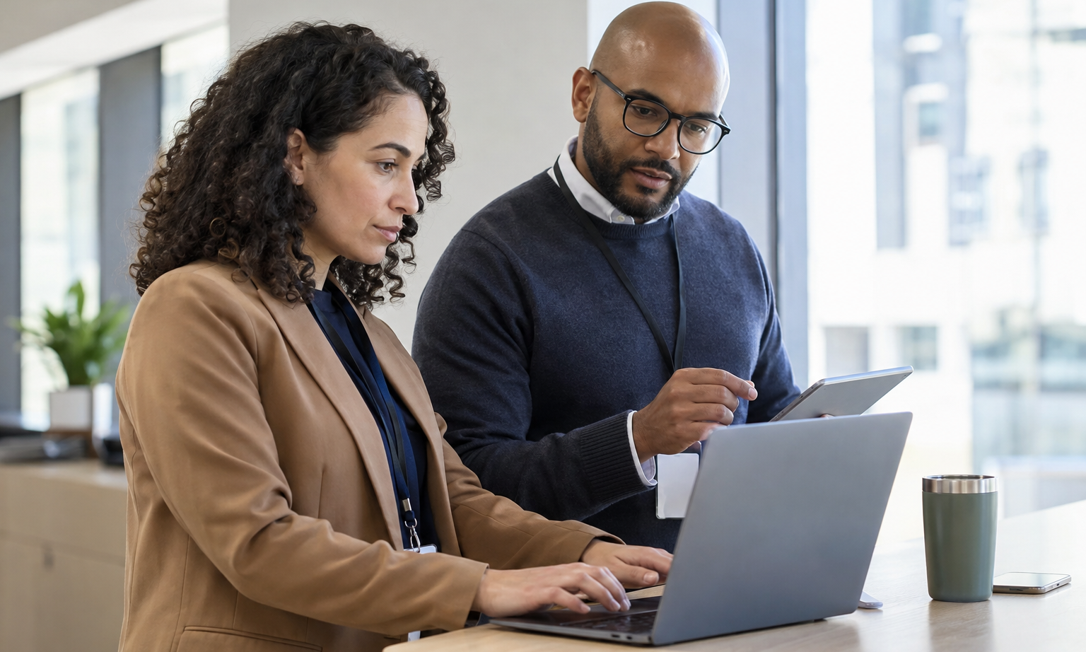 An IT security specialist and finance approver test workflow access permissions using two devices at a workstation.