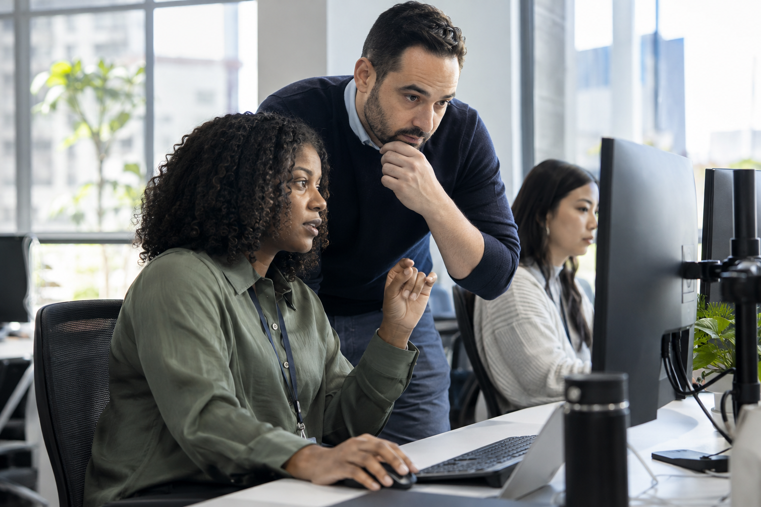 A customer-service team lead reviews an AI-assisted exception with a colleague working at a desktop.