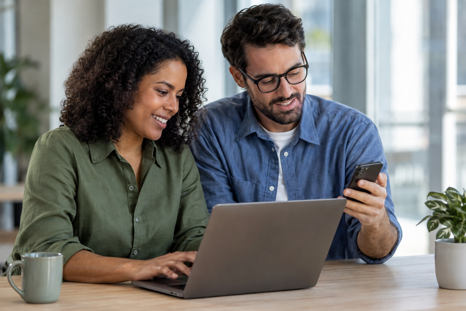 Two small-business colleagues test an automated appointment reminder using a laptop and phone at a shared workstation.