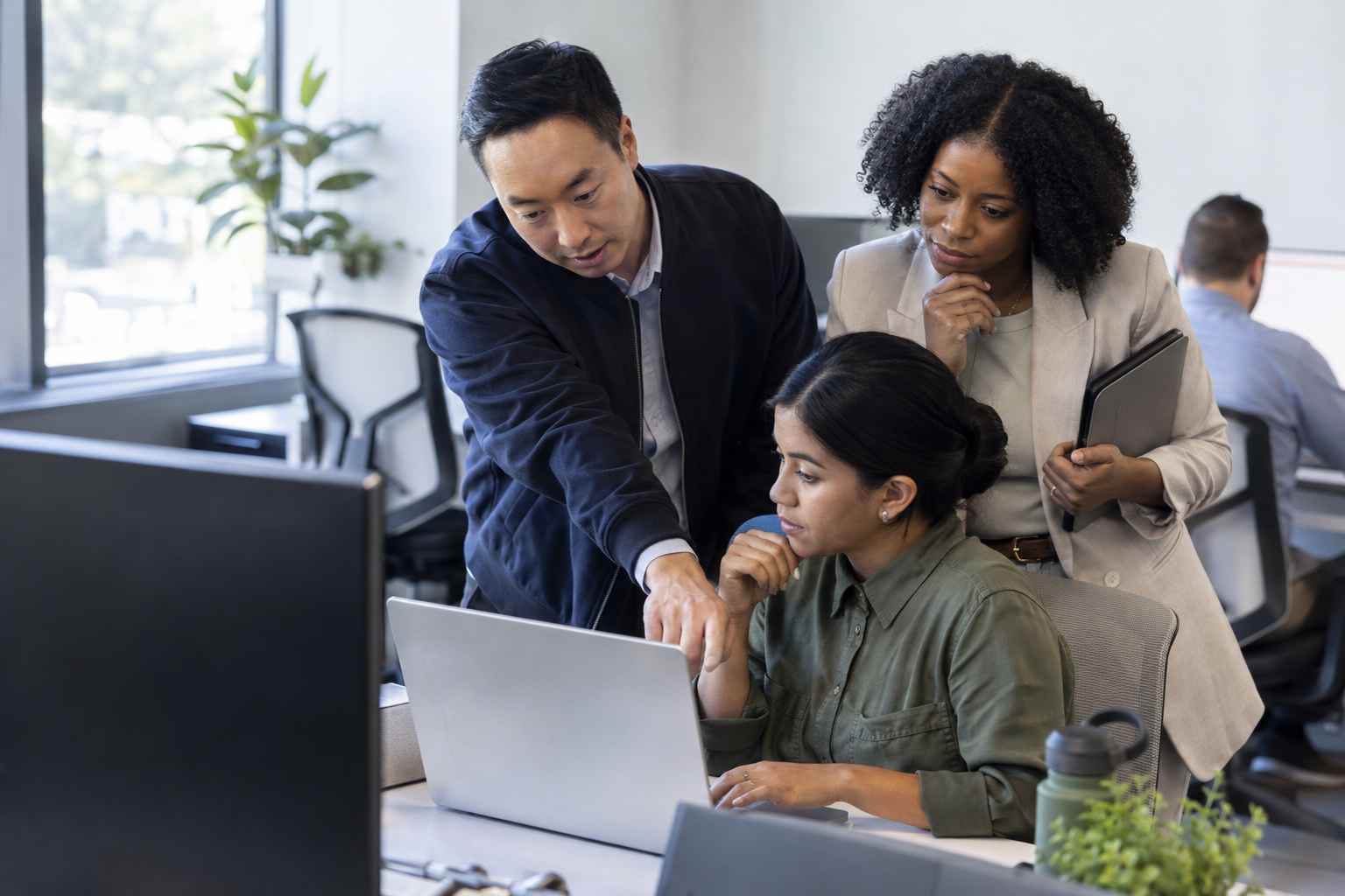 Three operations colleagues review a digitally routed exception at a laptop, with a team lead considering the next action.