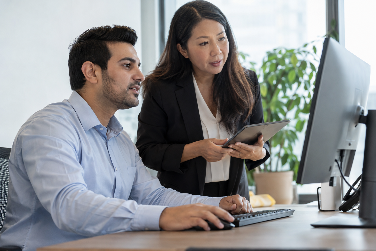 A finance analyst and operations manager use a desktop computer and tablet to review workflow automation savings and payback.
