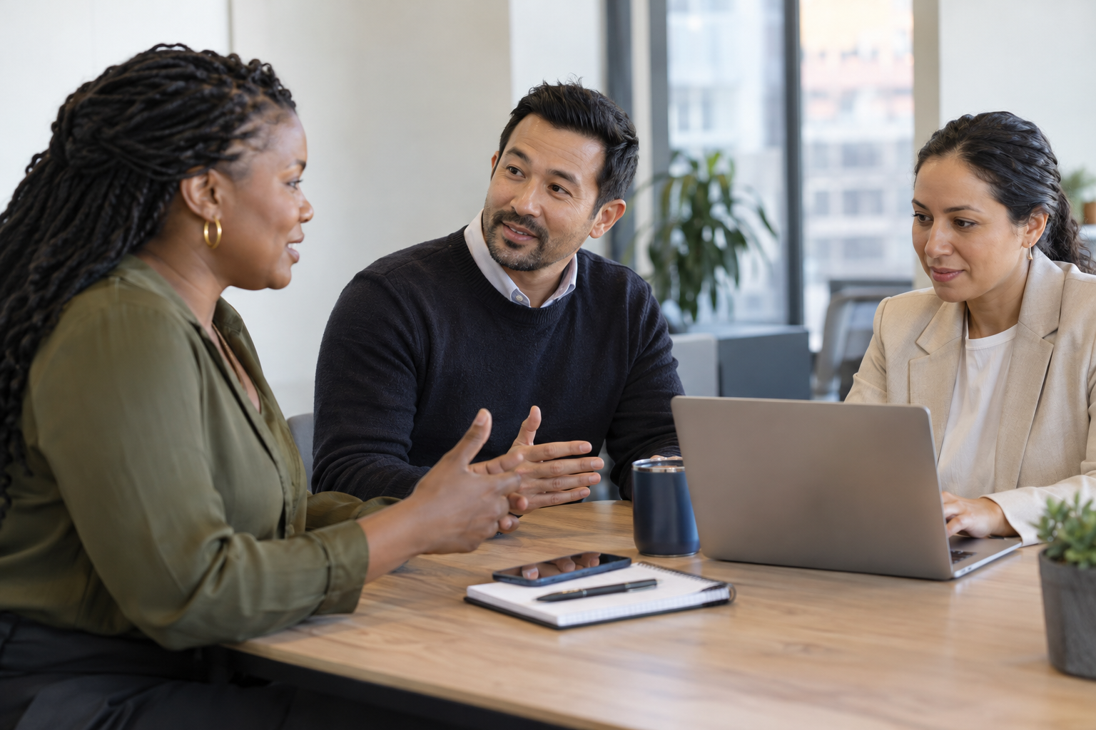 An HR lead updates a laptop record while an employee and their new manager discuss a reporting-line change.