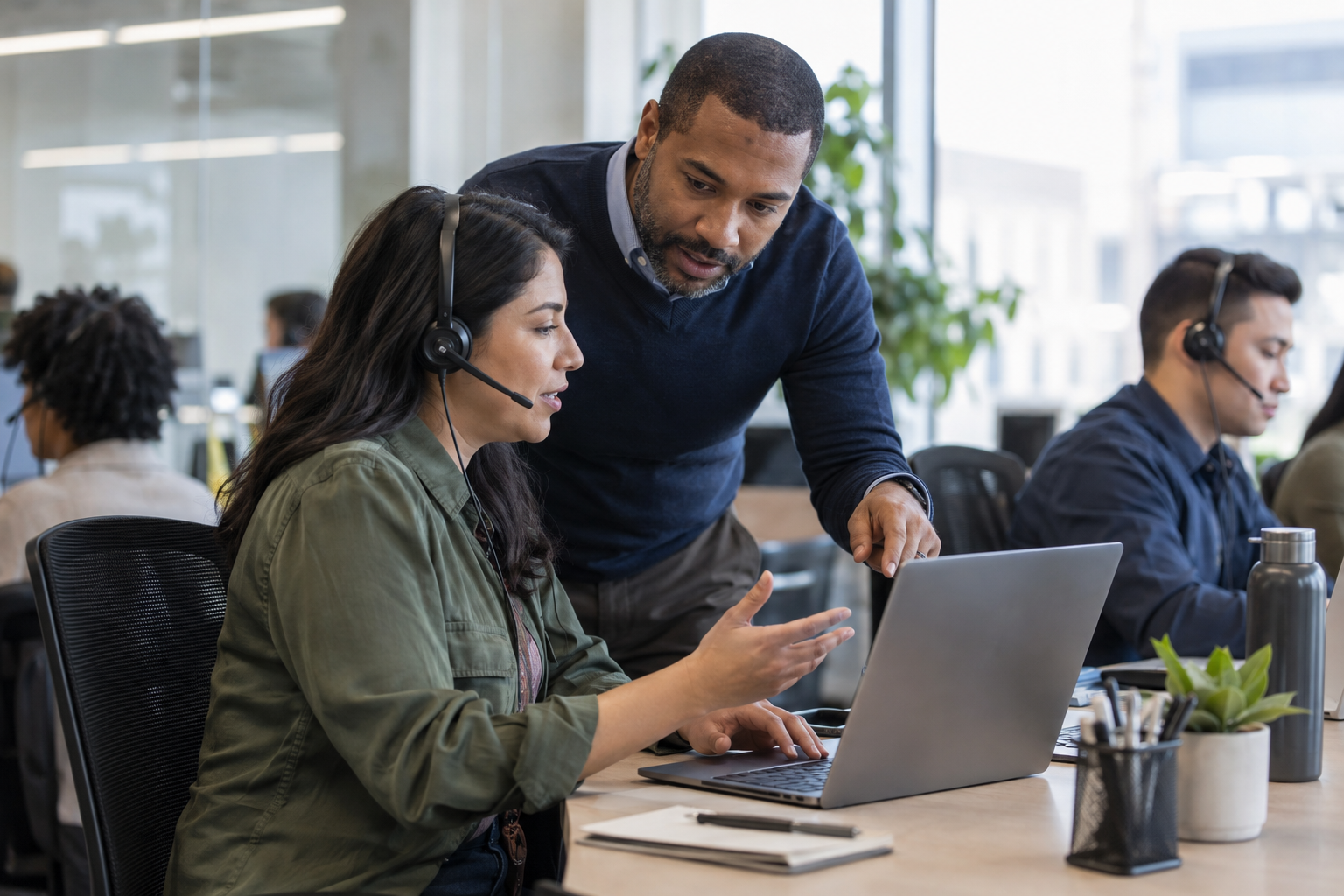 A customer-service specialist consults a supervisor at a laptop before approving an AI-assisted account adjustment.