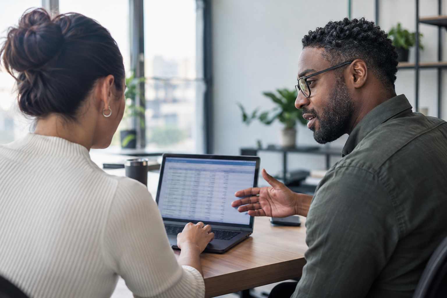 A finance analyst and AI engineering lead compare AI agent costs and verified task outcomes on a laptop.
