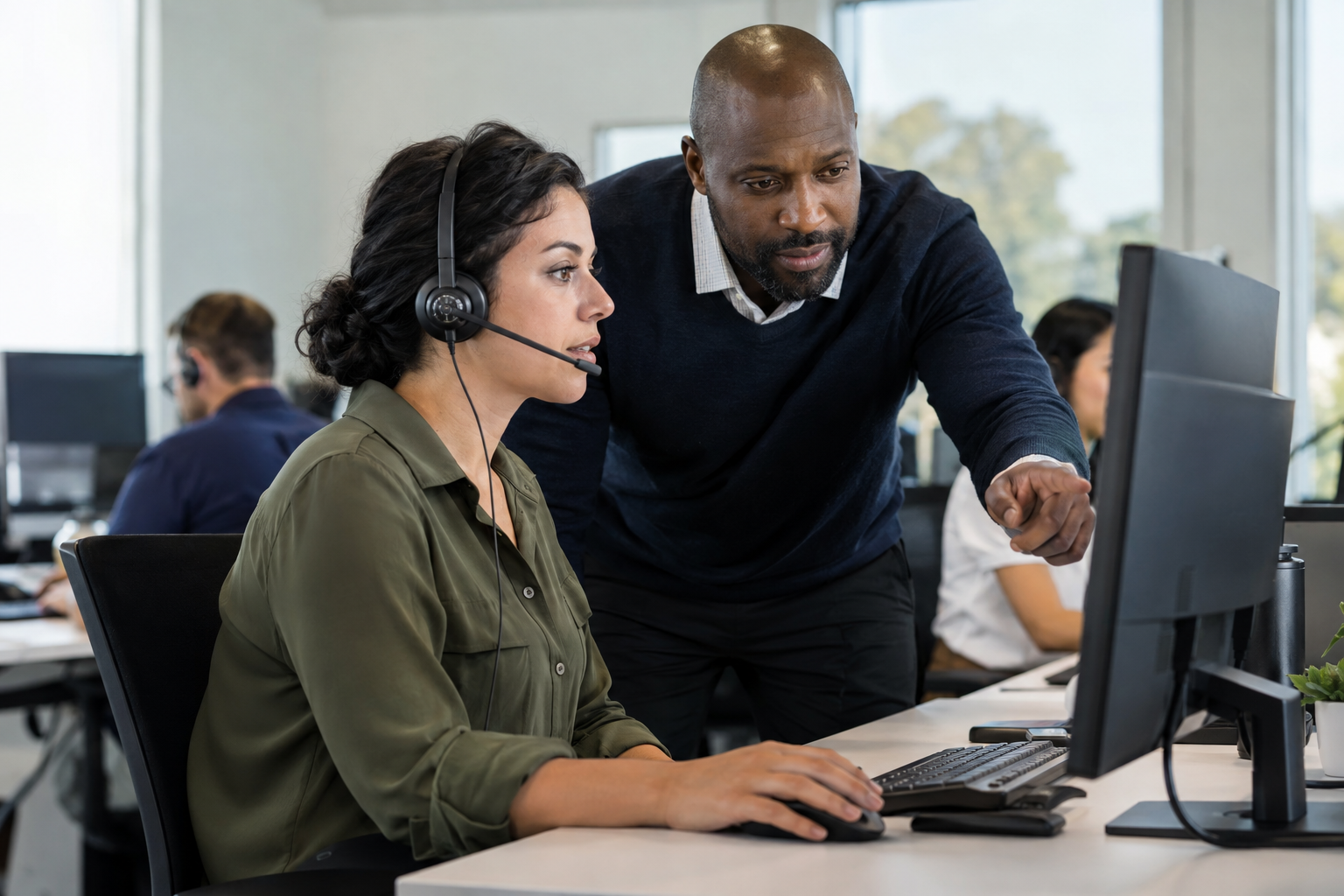 A customer support specialist reviews an AI-escalated case with a resolution lead beside a desktop computer.
