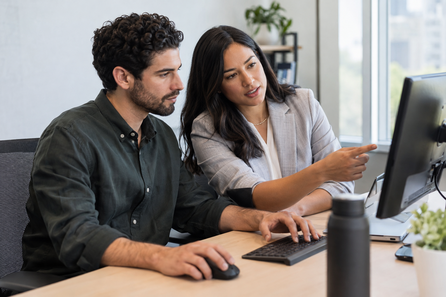 A recruiting analyst and talent acquisition lead review hiring funnel conversion rates together at a computer.