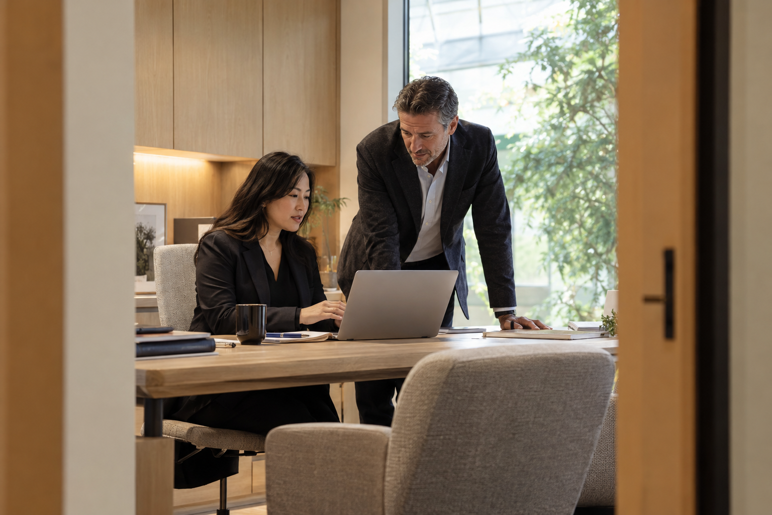 In a contemporary architecture practice’s quiet HR office, an Asian operations lead reviews pending leave requests on a single laptop while a department directo