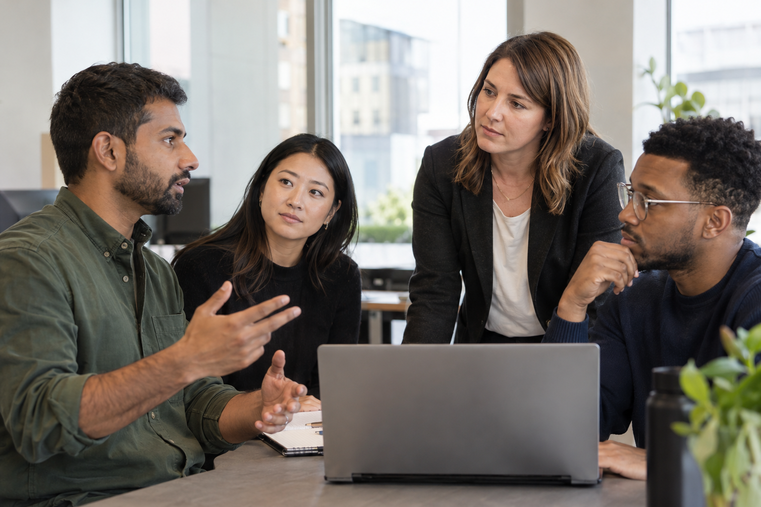 An engineering manager, project lead and two team members discuss release responsibilities around a laptop in a software office.