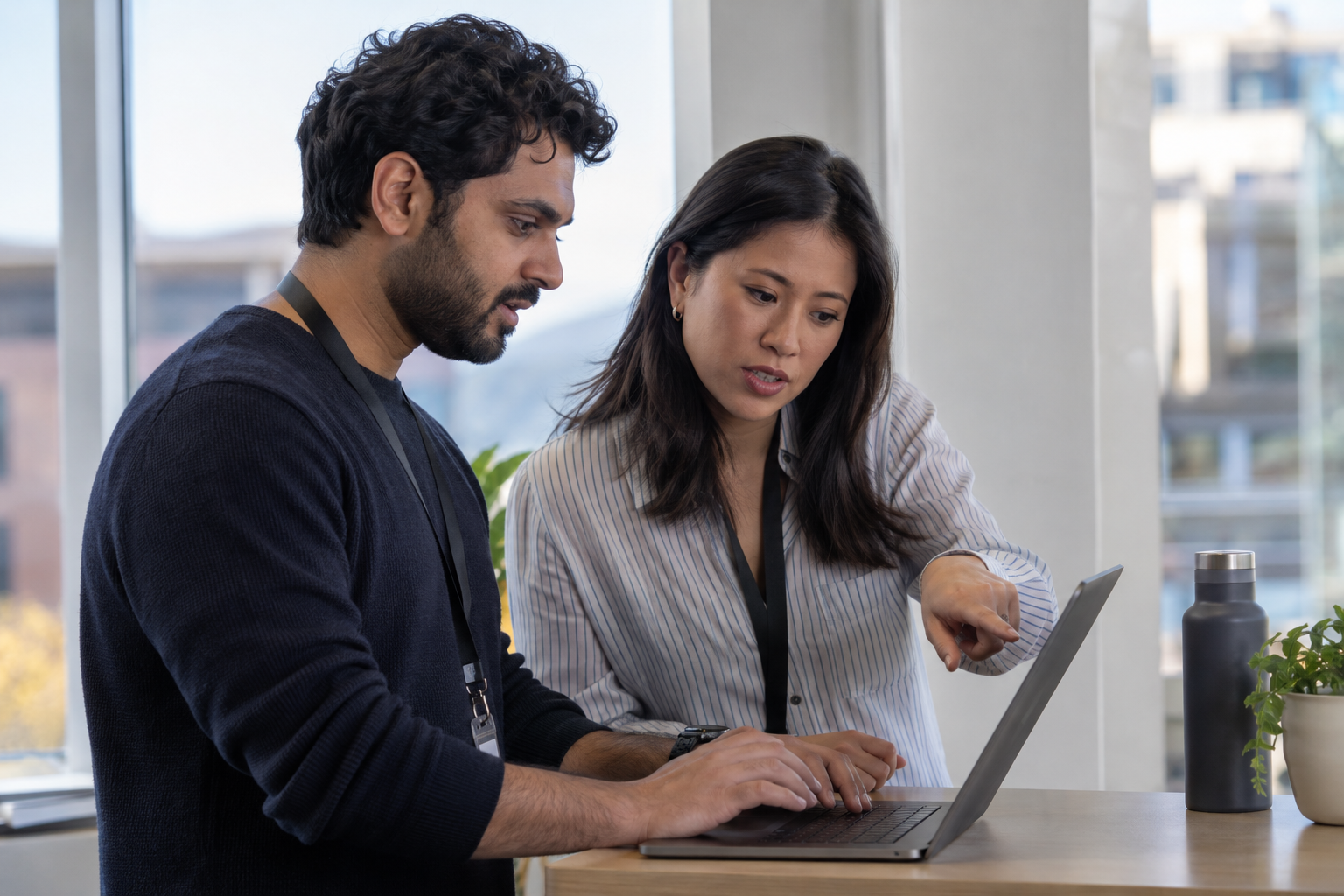An AI reliability engineer and business-process owner review a failed agent execution together on a laptop at a standing workstation.