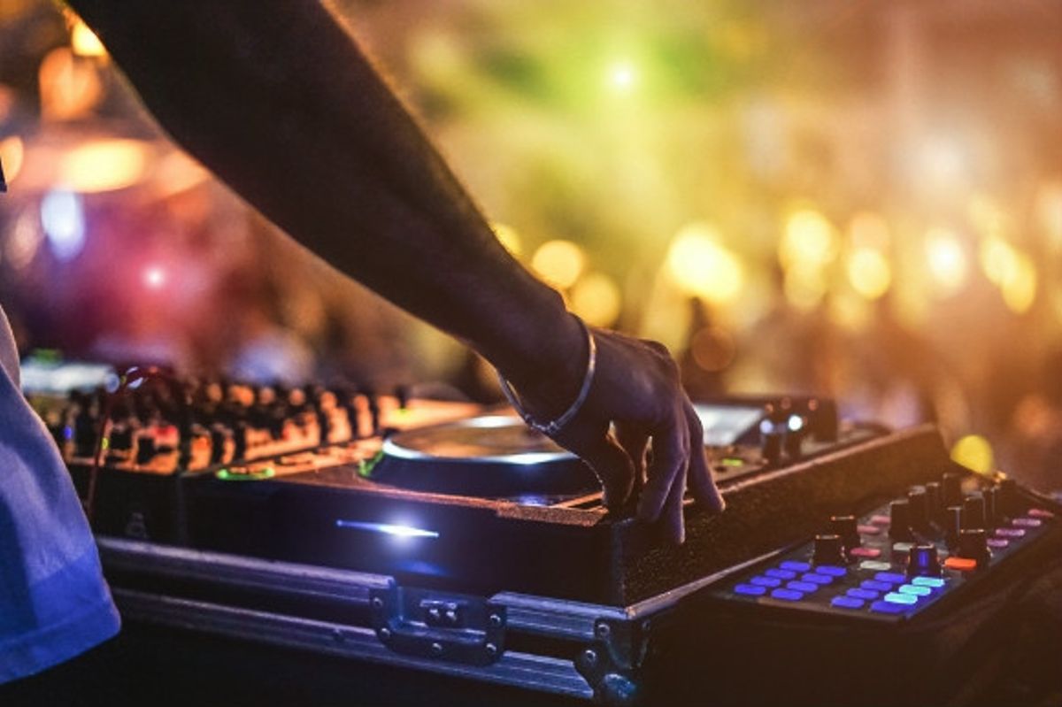 DJ spinning the decks and a wild crowd of people dancing in the background of a iconic club in Ibiza.