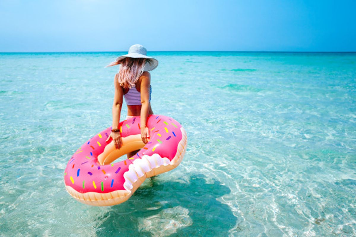 Young woman walking into the shallow sea water holding a doughnut inflatable 