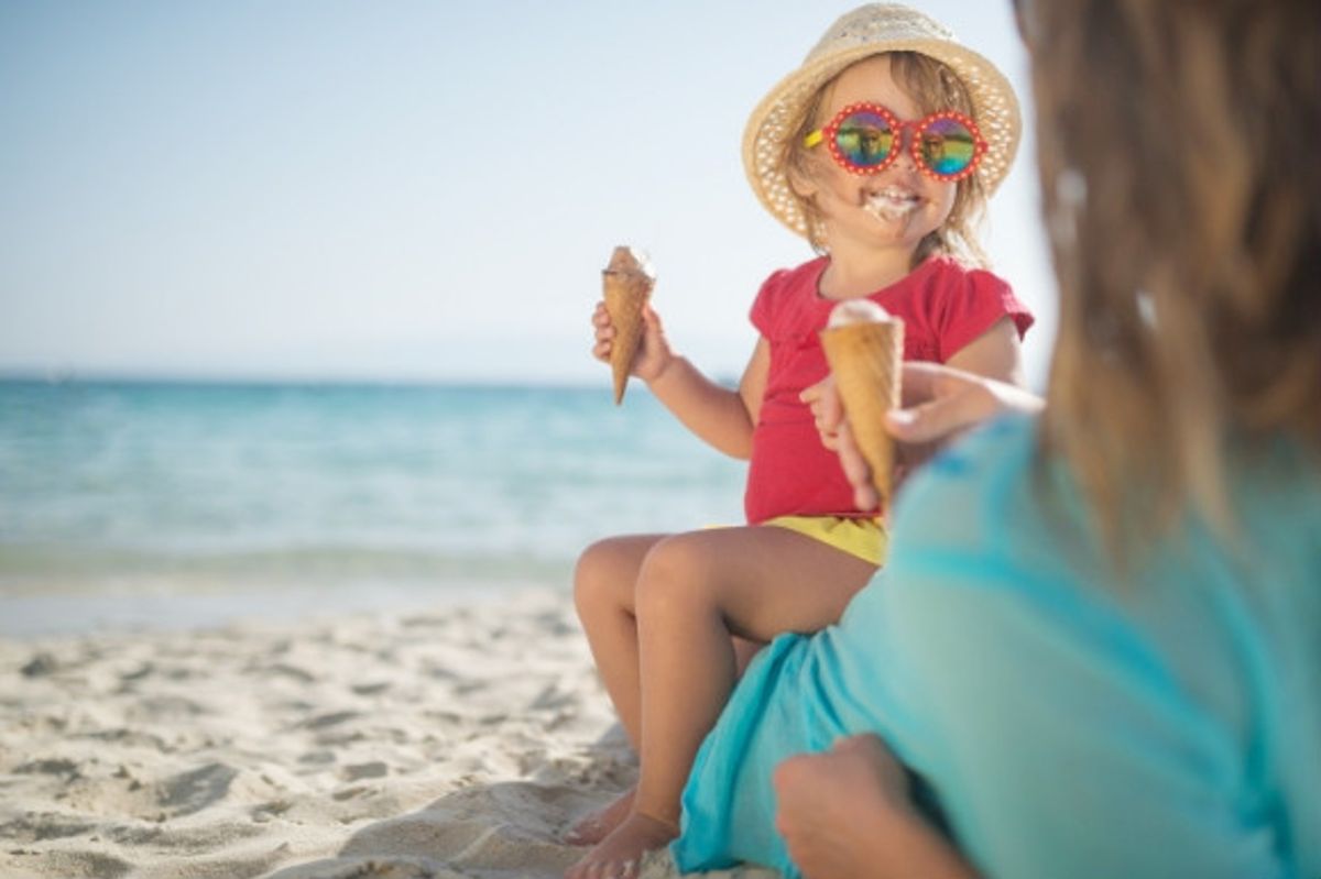Little girl eating a messy ice cream on the beach with her mum