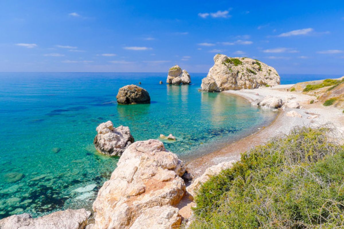 The iconic Rock of Aphrodite under Cyprus'' bright blue sky with azure waters and smaller rocks surrounding it
