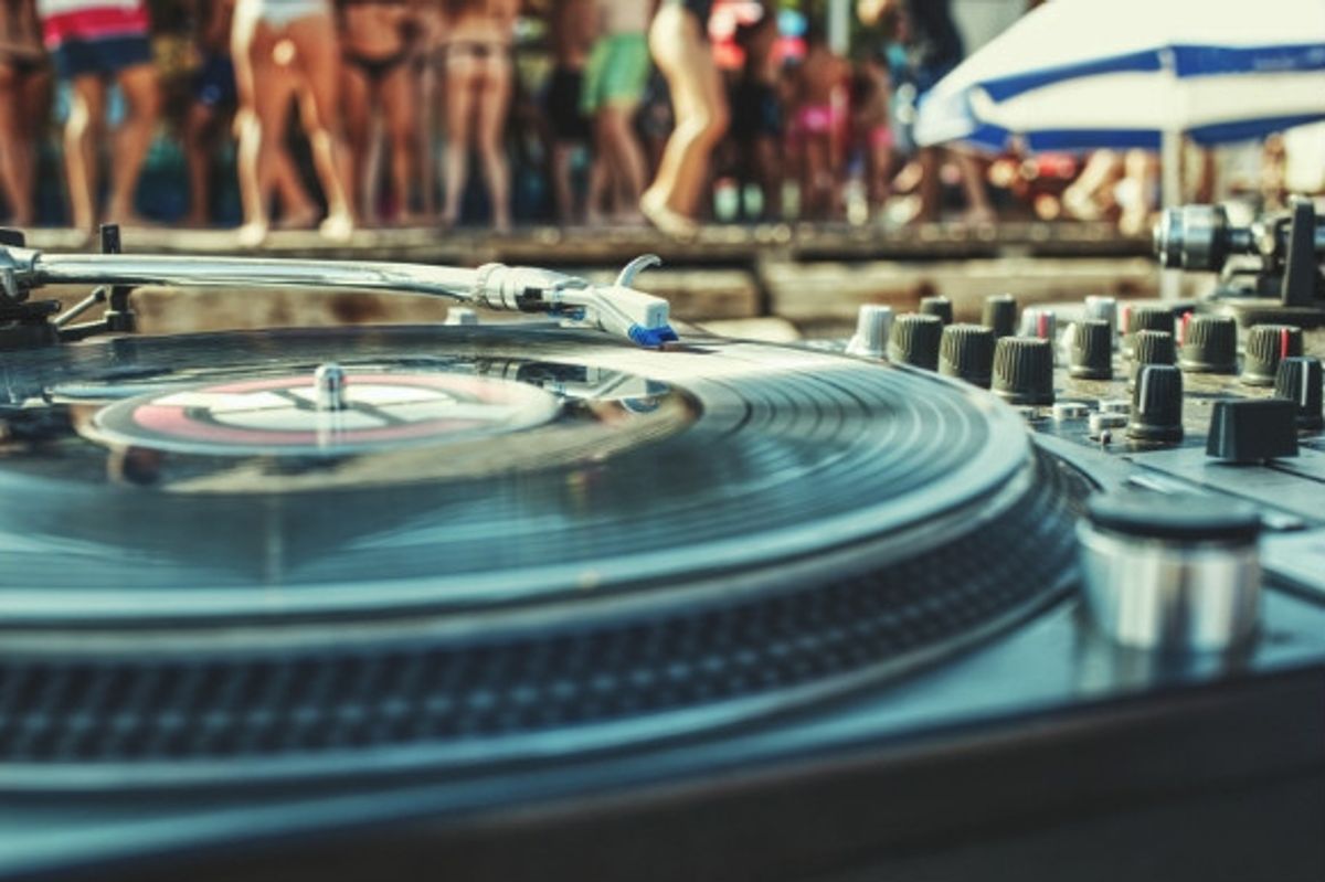 People dancing to the music coming from the DJ decks at a beach club.