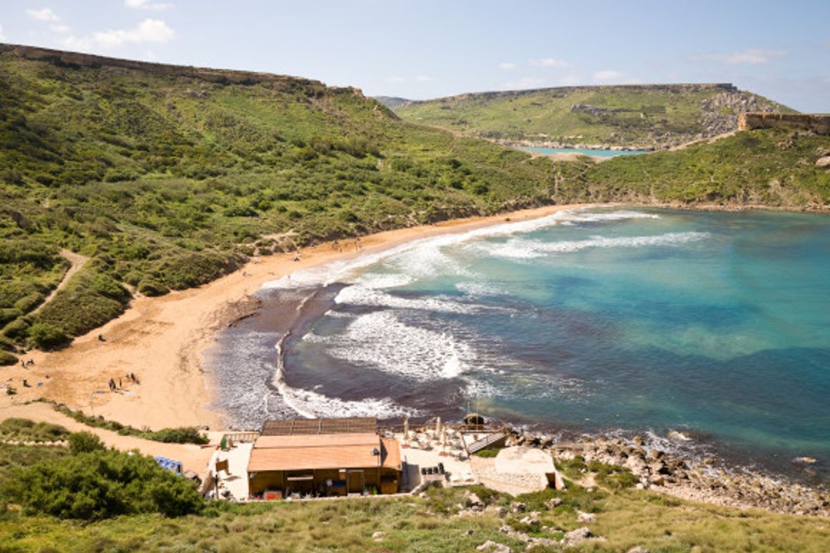 A view of Ghajn Tuffieha Beach with azure waters and greenery backing the sand.