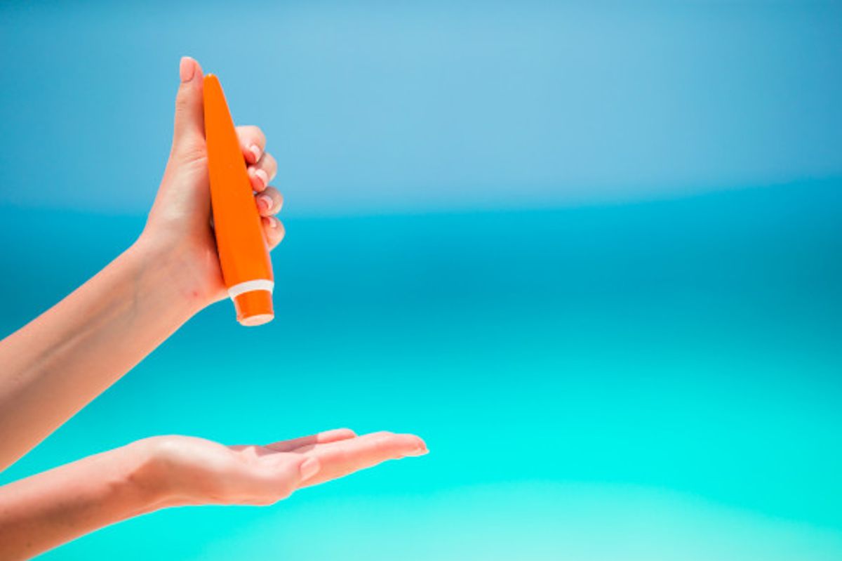 Woman applying sun cream against a bright blue background